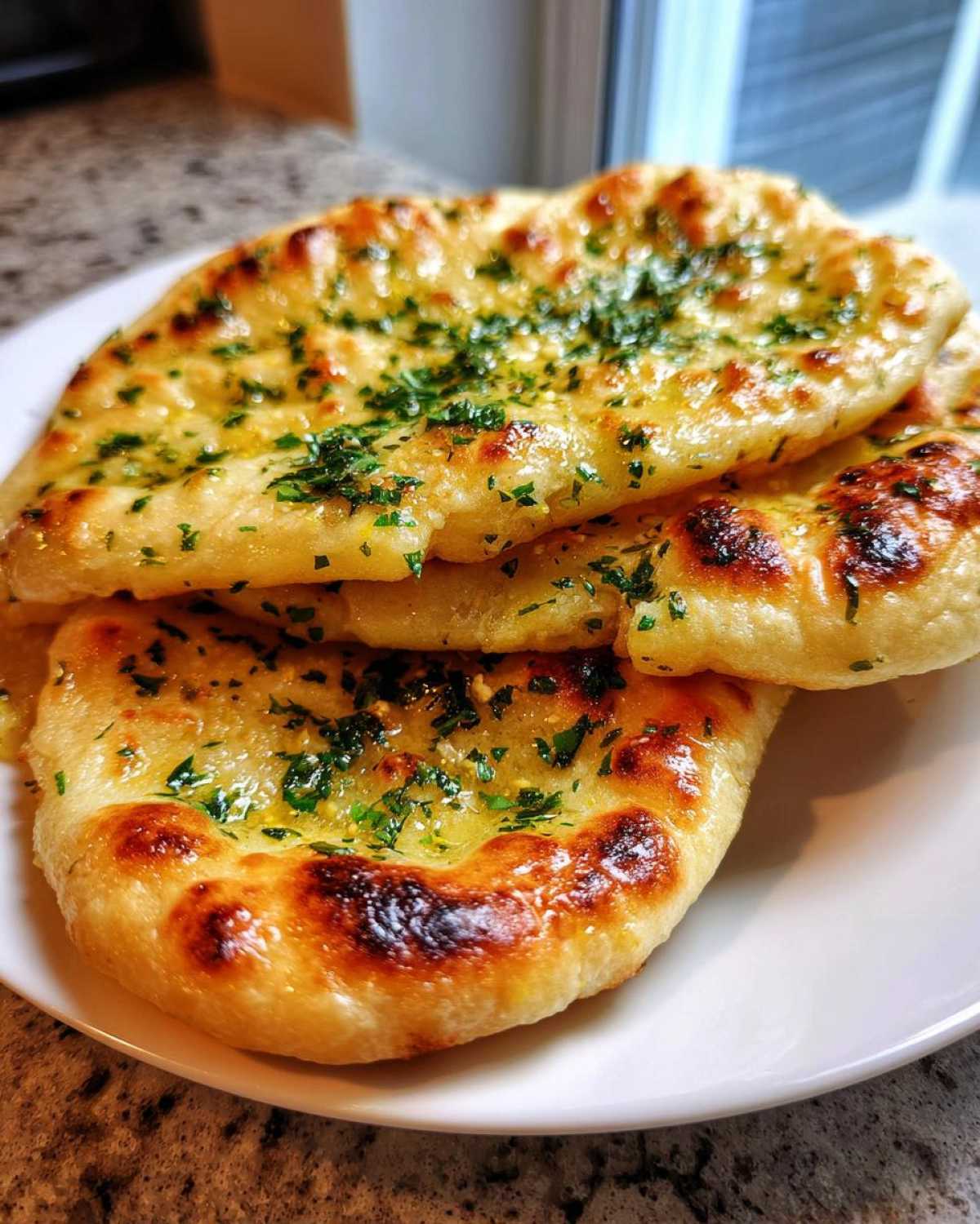 Close-up of stacked, soft naan bread brushed with melted butter and topped with chopped green herbs.
