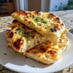 A stack of freshly baked, soft naan bread pieces garnished with chopped parsley, showing a fluffy interior.