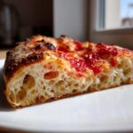 Close-up of a slice of pizza showing the airy, open crumb structure of the sourdough discard pizza dough.