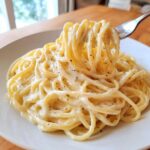 Close-up of spaghetti twirled on a fork, coated in rich homemade alfredo sauce and black pepper.