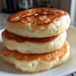 A close-up stack of three thick, fluffy pancakes showing golden brown, perfectly cooked tops.