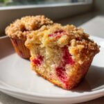 A strawberry muffin cut in half showing the moist interior filled with bright red strawberries and topped with golden brown streusel, part of our amazing strawberry muffins recipe.