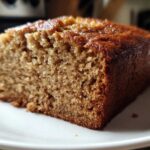 Close-up of a moist, golden-brown slice of sugar free banana bread on a white plate.