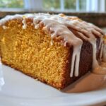 A close-up of a moist slice of sweet potato pound cake topped with thick vanilla glaze dripping down the sides.
