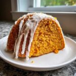 A close-up of a moist slice of orange sweet potato pound cake topped with thick white icing drizzle.
