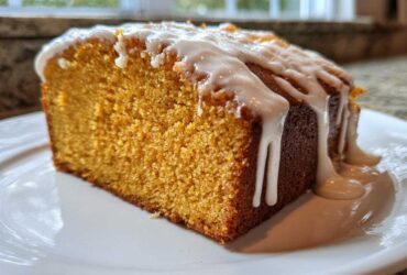 A close-up of a moist slice of sweet potato pound cake topped with thick vanilla glaze dripping down the sides.