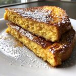 Two thick, golden slices of easy french toast stacked on a white plate, dusted generously with powdered sugar and drizzled with syrup.