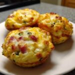 Close-up of three freshly baked Egg Muffin Cups topped with melted cheese and visible pieces of ham.