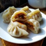 Close-up of steamed Traditional Chinese Dumplings, one cut open to show the savory filling.