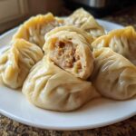 A plate of freshly steamed Traditional Chinese Dumplings, one cut open to show the savory meat filling.