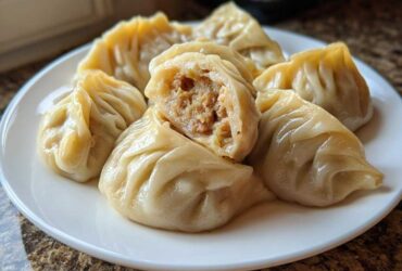 A plate of freshly steamed Traditional Chinese Dumplings, one cut open to show the savory meat filling.