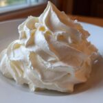 Close-up of a perfectly piped swirl of creamy vanilla buttercream frosting on a white plate.
