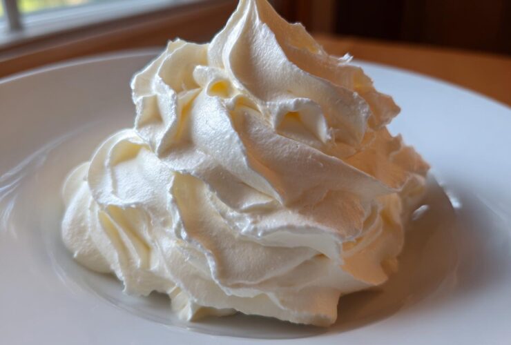 Close-up of a perfectly piped swirl of creamy vanilla buttercream frosting on a white plate.