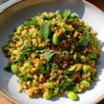 Close-up of a vibrant crispy rice salad mixed with bright green edamame beans and fresh mint leaves.