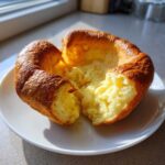 A golden brown, perfectly risen Yorkshire pudding split open to show its fluffy, airy interior.