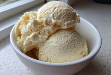 Close-up of creamy, pale yellow banana ice cream scooped into a white bowl near a window.