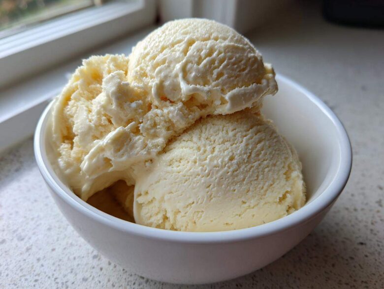 Close-up of creamy, pale yellow banana ice cream scooped into a white bowl near a window.