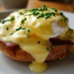 Close-up of a perfectly prepared eggs benedict featuring a poached egg, rich hollandaise sauce, and chives on toast.