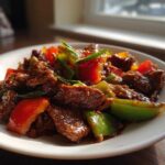 A close-up of delicious pepper steak featuring tender beef strips and vibrant red and green bell peppers coated in a savory sauce.