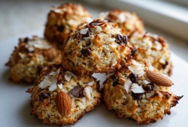 A stack of golden brown almond joy cookies topped with chocolate chips, shredded coconut, and whole almonds.