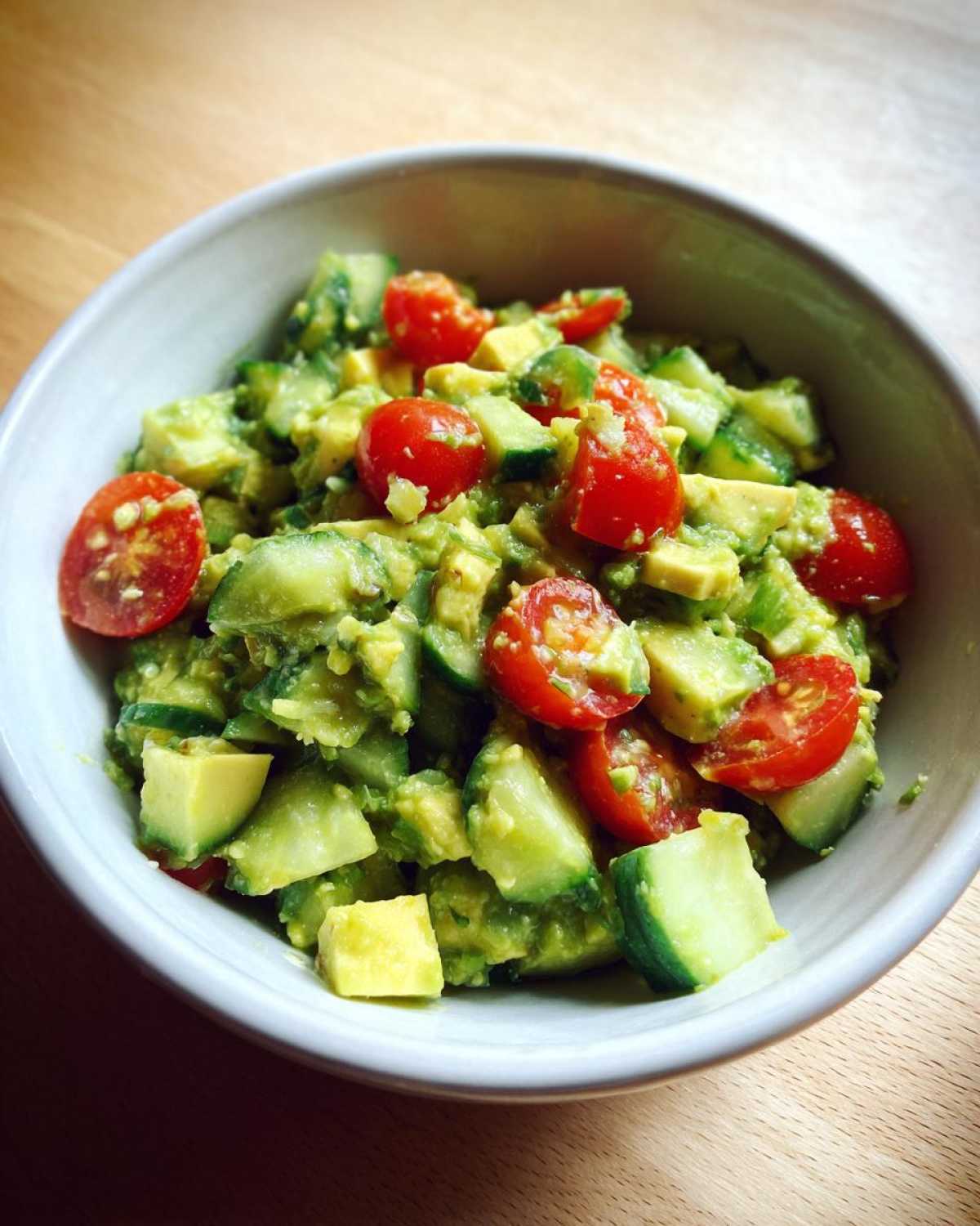 Close-up of a vibrant avocado salad mixed with diced cucumber and halved cherry tomatoes.