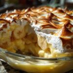A close-up view of a serving dish filled with creamy banana pudding, layered with sliced bananas and topped with perfectly toasted meringue.