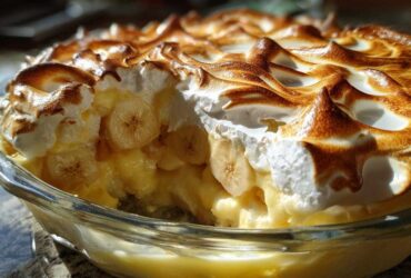 A close-up view of a serving dish filled with creamy banana pudding, layered with sliced bananas and topped with perfectly toasted meringue.