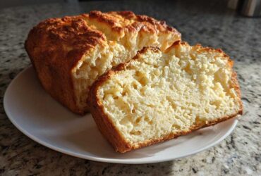 A golden-brown loaf of homemade beer bread, partially sliced, showing the fluffy interior texture.