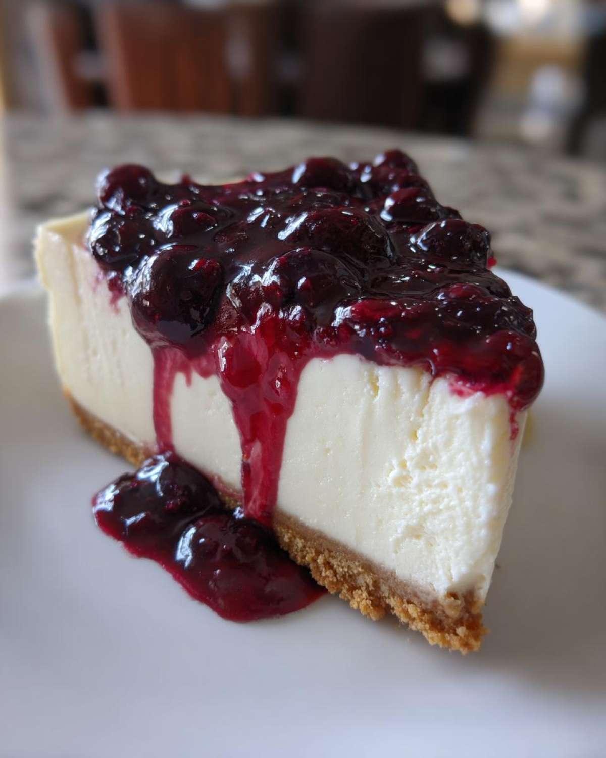 A close-up of a perfect slice of creamy blueberry cheesecake with rich berry topping dripping down the side.