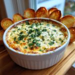 A hot, cheesy baked bread dip topped with fresh parsley, served with toasted bread slices arranged around the bowl.