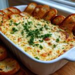 A baked, cheesy bread dip topped with parsley, served hot in a white dish surrounded by toasted bread slices.
