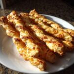A plate of freshly baked, golden brown, twisted cheese straws recipe sticks glistening in sunlight.