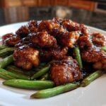 Close-up of saucy glazed chicken pieces served over bright green beans, featuring the main chicken and green beans ingredients.