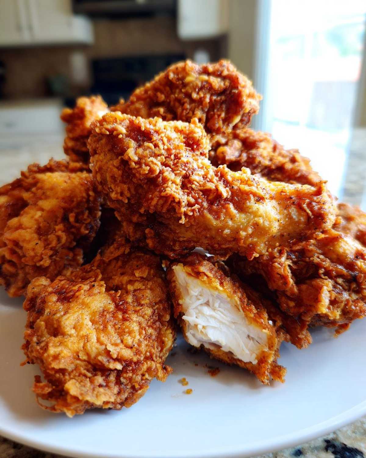 A pile of golden brown, crispy fried chicken wings on a white plate, one piece cut open showing the white meat.