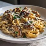A close-up of creamy mushroom pasta made with fettuccine, topped with sautéed mushrooms and grated Parmesan cheese.