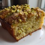Close-up of a moist slice of pistachio coffee cake topped with chopped pistachios and sugar.