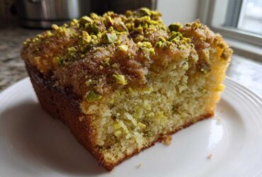 Close-up of a moist slice of pistachio coffee cake topped with chopped pistachios and sugar.