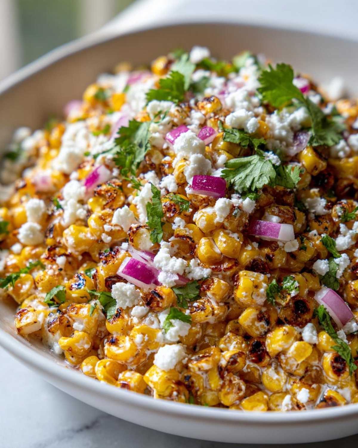 Close-up of vibrant street corn salad featuring charred corn kernels, crumbled white cheese, red onion, and cilantro.