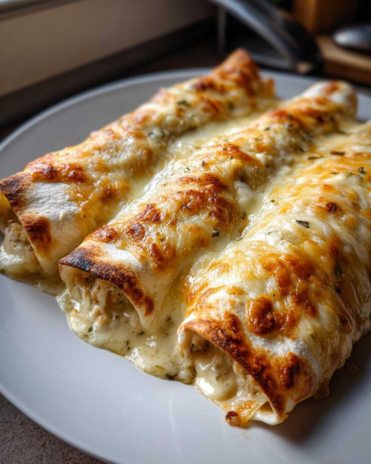 Close-up of three baked white chicken enchiladas covered in bubbling, melted cheese.
