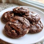 Close-up of five rich, dark chocolate Andes mint cookies piled on a white plate with melted chocolate chunks.