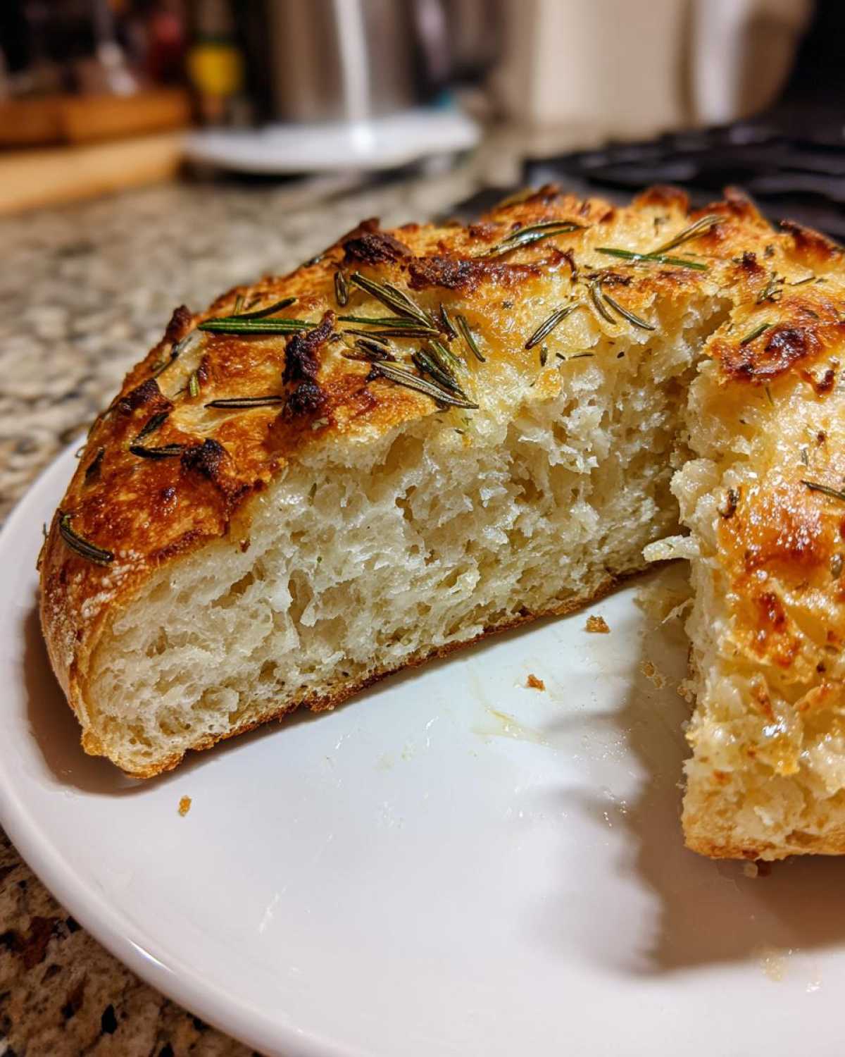 Close-up of sliced artisan bread showing the airy interior crumb and golden, rosemary-topped crust.