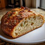Cross-section of a golden-crusted artisan bread topped with rosemary and cheese, showing an airy interior.