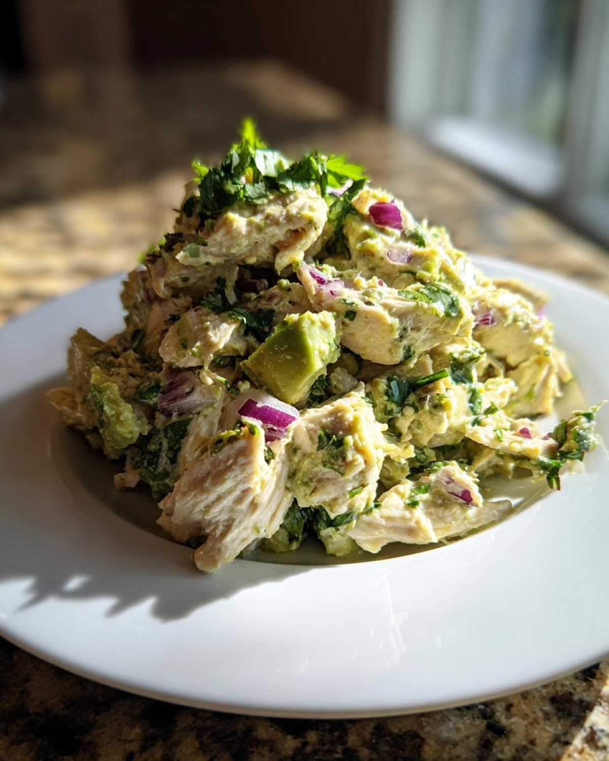 A mound of creamy avocado chicken salad mixed with chunks of avocado and red onion, topped with fresh cilantro.