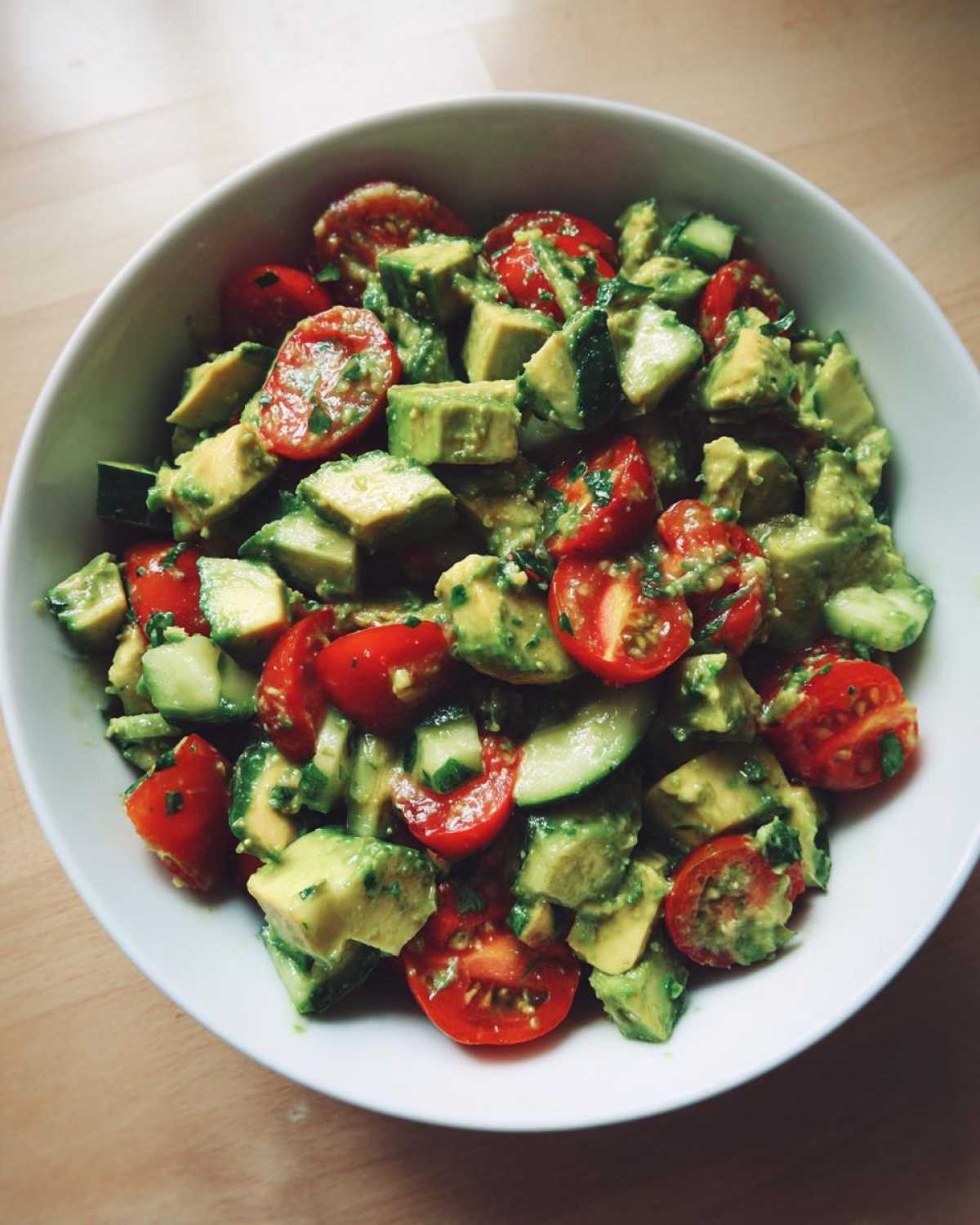 Close-up of a vibrant avocado salad featuring diced avocado, halved cherry tomatoes, and cucumber chunks.