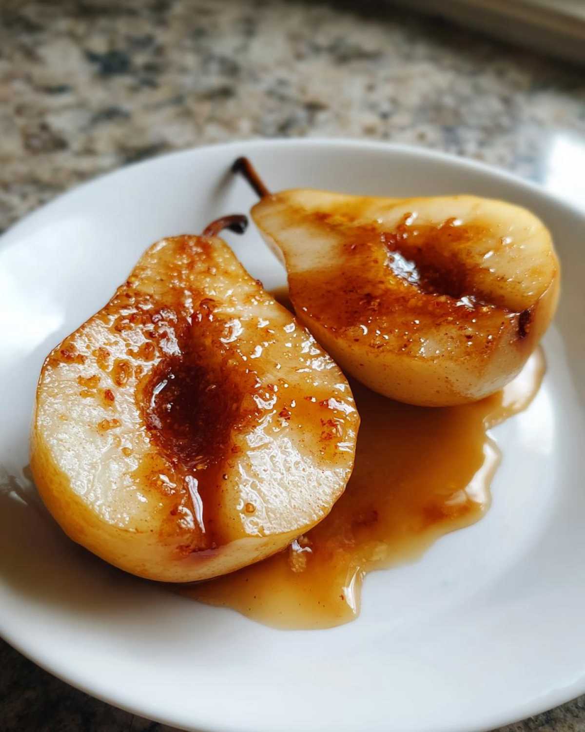 Two halves of sweet, caramelized baked pears drizzled with syrup, served on a white plate.