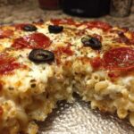 A close-up, cross-section view of a baked pizza pasta casserole, showing macaroni noodles mixed with cheese and topped with pepperoni and olives.