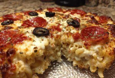 A close-up, cross-section view of a baked pizza pasta casserole, showing macaroni noodles mixed with cheese and topped with pepperoni and olives.