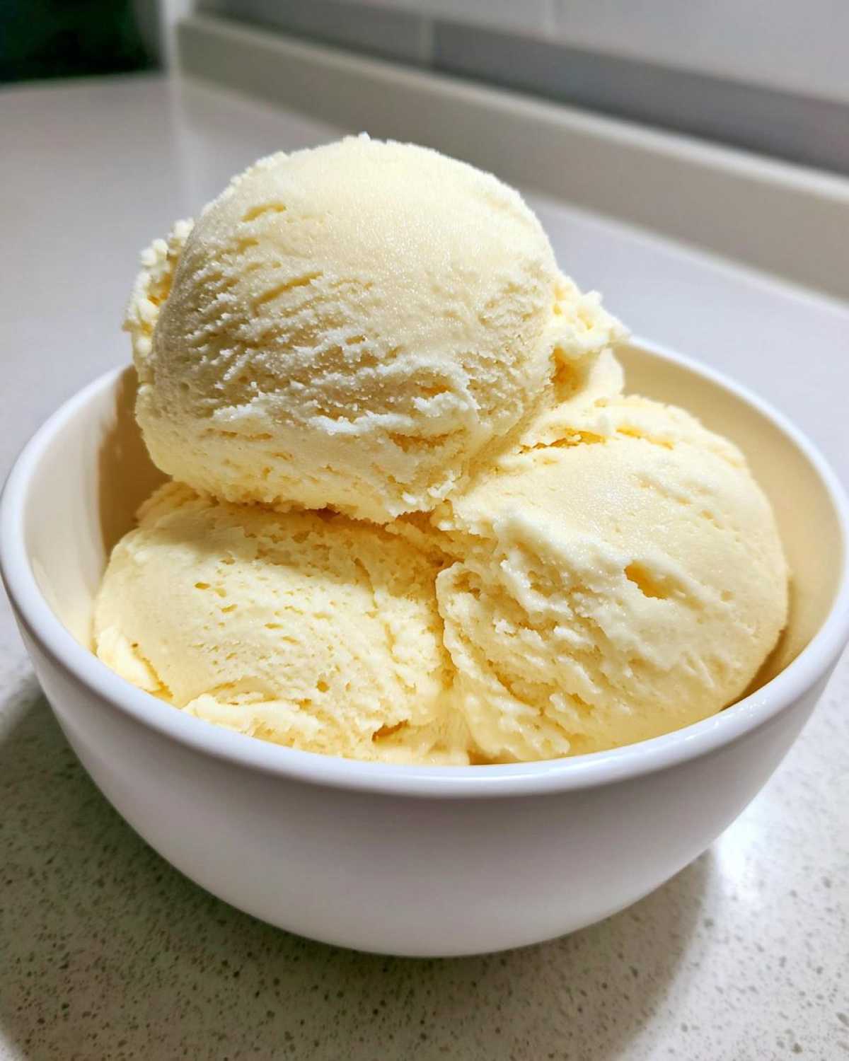 Three scoops of creamy, pale yellow banana ice cream served in a white bowl.