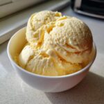 Three scoops of creamy, pale yellow banana ice cream served in a small white bowl.