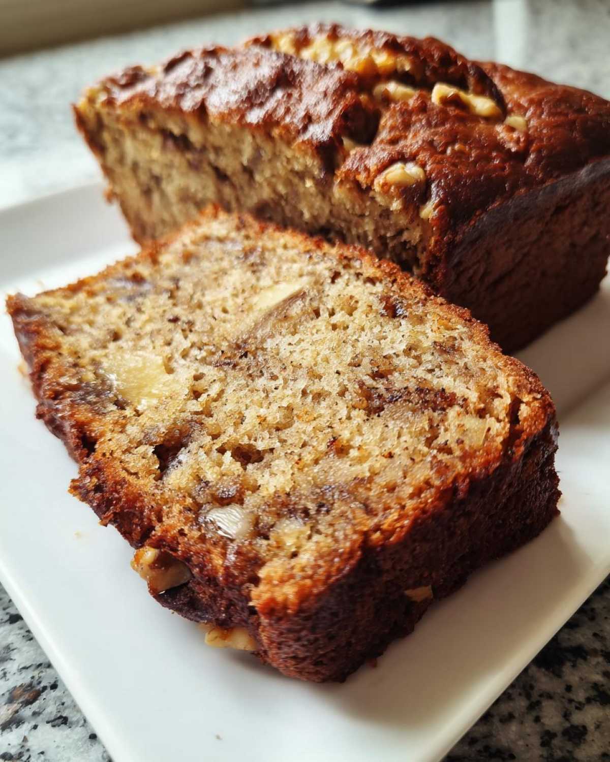 Close-up of a moist slice of the best banana bread, showing walnuts and a dark, caramelized crust.